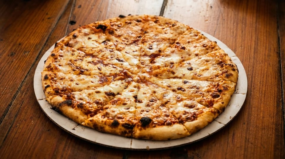 A whole cheese pizza, cut into slices, on a cardboard round on a wooden table.