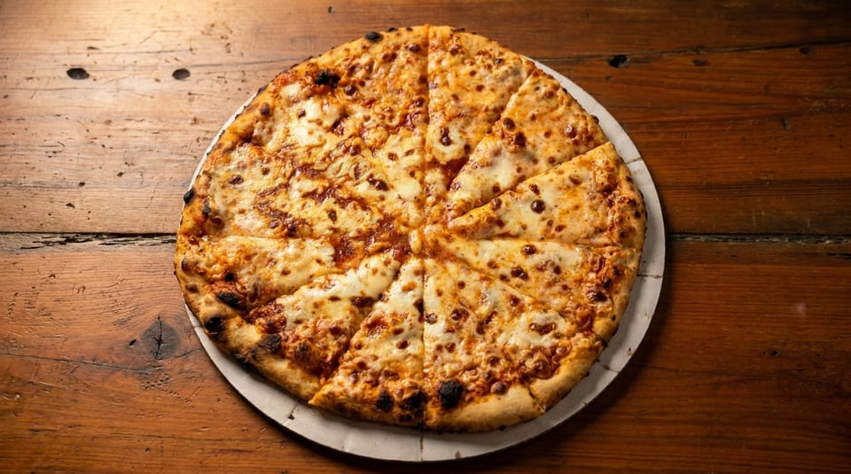 A freshly baked, sliced cheese pizza with a crispy crust sits on a rustic wooden table.
