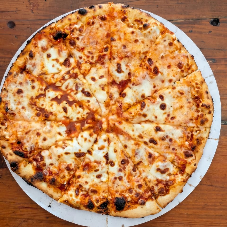 A whole, sliced cheese pizza with a crispy crust sits on a rustic wooden table.