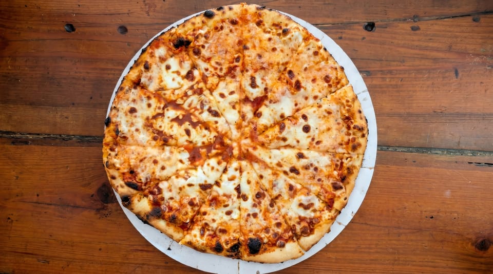 A whole, sliced cheese pizza with a crispy crust sits on a rustic wooden table.